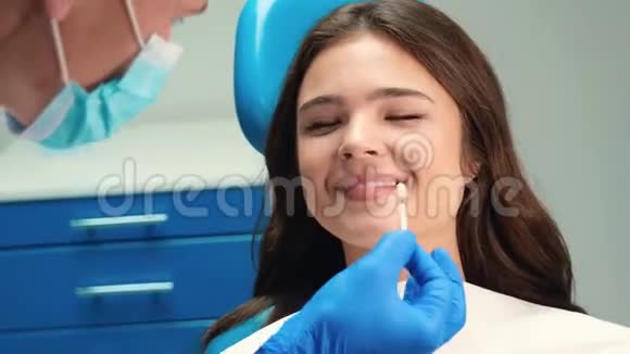 微笑的黑发病人在牙科诊所预约的妇女戴着口罩和手套的牙医在视频的预览图