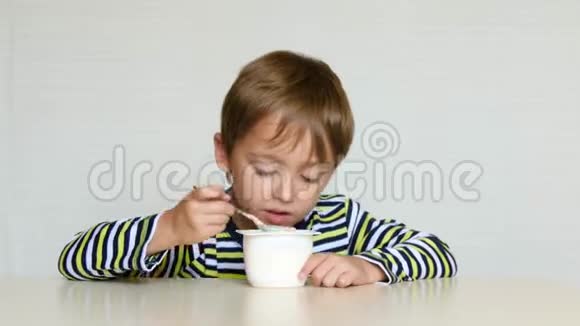 男孩坐在桌子旁从罐子里吃酸奶体验情绪快乐快乐快乐儿童食品视频的预览图