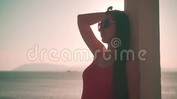 一个穿着红色的一件泳衣和眼镜的漂亮女孩站在海滩上穿着白色的混凝土凉亭视频的预览图