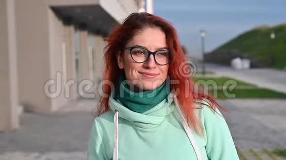 一个女人穿着舒适温暖的运动服和围巾走在街上微笑的肖像快乐的红发女孩走进来视频的预览图