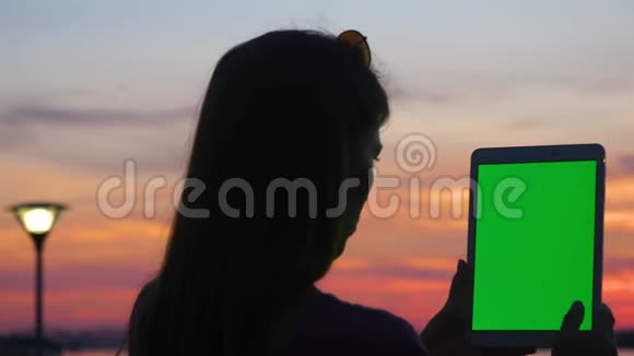 女人在日落时拿着数字平板电脑视频的预览图