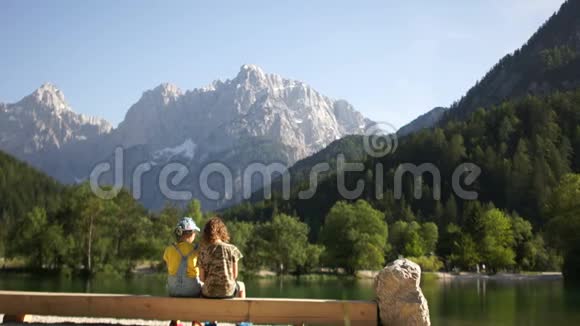 男孩和女孩坐在山上背景的一个山湖岸边的长凳上暑假兄弟视频的预览图