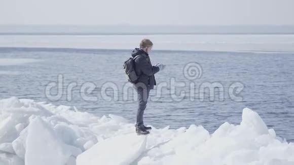 自信的男人穿着一件温暖的外套站在冰川上挺直了头发看着远处奇妙的大自然视频的预览图