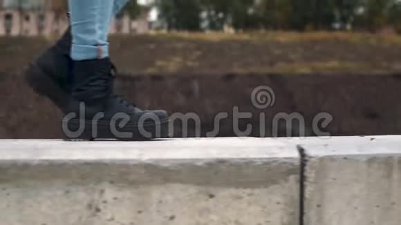 一个女人穿着黑色的大靴子沿着混凝土栅栏走近u视频的预览图