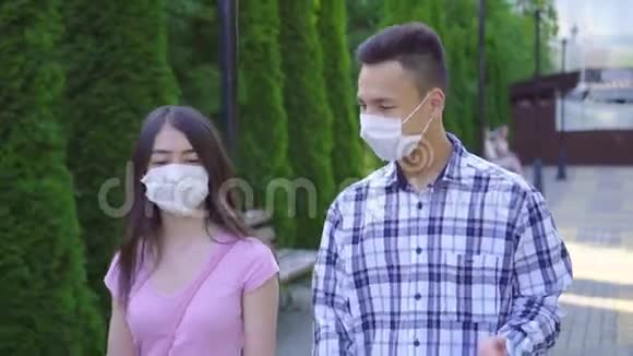 两个戴着医用口罩的亚洲青年学生走在街上近距离交谈视频的预览图