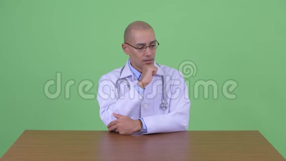 压力重重的秃头多民族男医生在办公桌后思考视频的预览图
