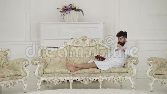 留着胡子和胡子的人喜欢早上躺在豪华沙发上穿着浴衣喝咖啡看书的人视频的预览图