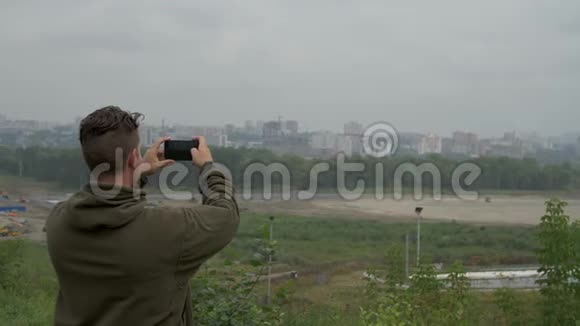 年轻人站在一个烟雾弥漫的城市在电话里拍了一张城市的照片视频的预览图