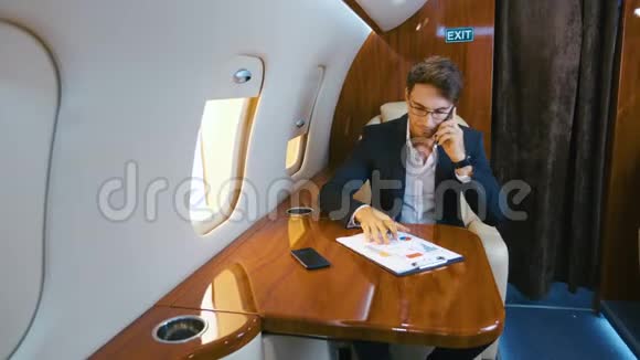 忙碌的商人在私人喷气式飞机上飞行时处理文件和在手机上交谈飞机视频的预览图