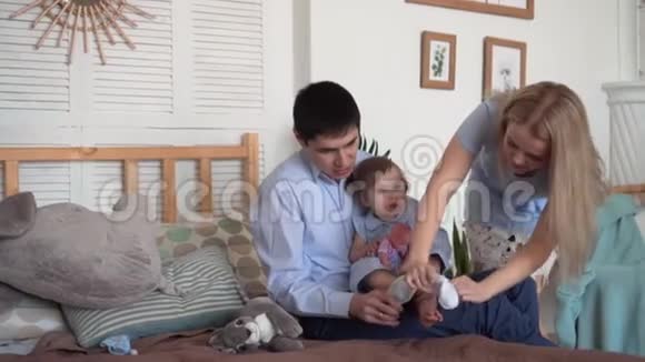 一家人在床上微笑爸爸妈妈和他们的小女儿一起穿袜子视频的预览图