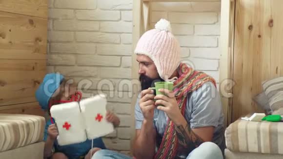 戴着帽子和围巾的病人喝茶一个穿着军装的男孩从急救箱里给他送药父亲视频的预览图