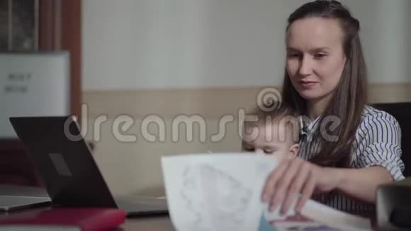忙碌的年轻母亲在家工作孩子在她的大腿上男孩用钢笔在母亲文件上画画女人是视频的预览图