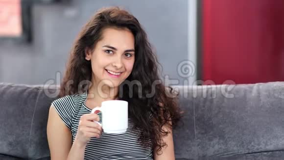 美丽的白种人年轻女性卷发在家放松手里拿着一个大白杯视频的预览图