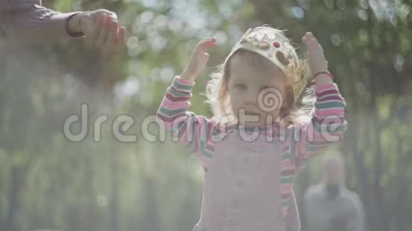 肖像可爱的小女孩在皇冠上的前景绿色公园的背景皇冠太大了视频的预览图
