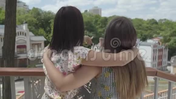 两个可爱的年轻女子站在户外拥抱和交谈欣赏美丽的城市景观女朋友视频的预览图