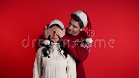 男人闭上女朋友的眼睛然后给她惊喜戴着红色圣诞帽的情侣视频的预览图