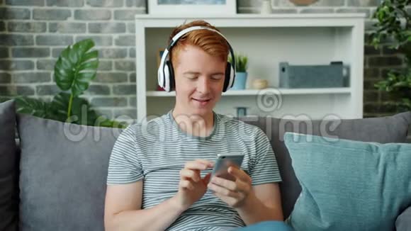 快乐的人在家通过耳机听音乐和使用智能手机视频的预览图