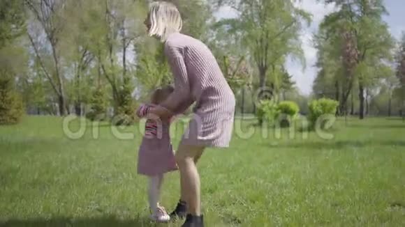 春日美丽的年轻母亲用手把女儿纺在大自然上在公园里玩耍的女人和小孩视频的预览图