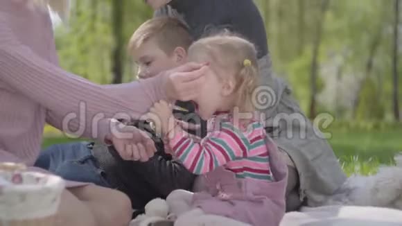描绘了两个可爱的年轻可爱的母亲和他们的孩子坐在绿色的神奇公园的毯子上的自然春天的一天视频的预览图