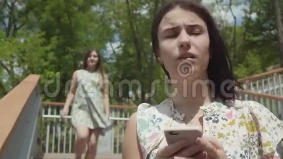 漂亮可爱的小女孩坐在前台在手机上发短信无忧无虑的朋友在她后面跑视频的预览图