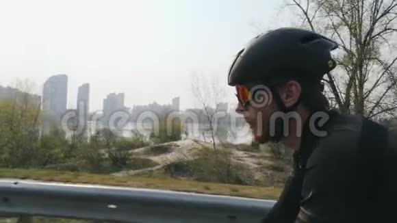 年轻的骑自行车的人留着胡子戴着太阳镜戴着头盔穿着黑色衣服骑自行车特写侧视图自行车概念慢m视频的预览图