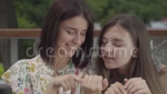 两个漂亮的女孩坐在户外一起谈论新的指甲展示手指和指甲女朋友的谈话视频的预览图