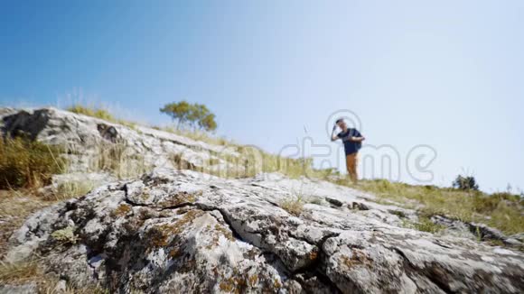 夏日迎着蓝天漫步在岩石坡上的年轻成年徒步旅行者视频的预览图