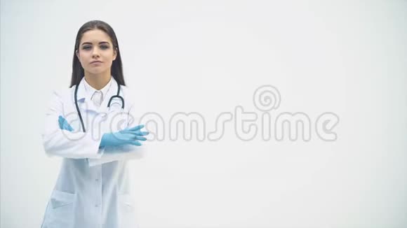 年轻的女医生出现在白色的背景下看着镜头微笑着摆姿势双手合十视频的预览图