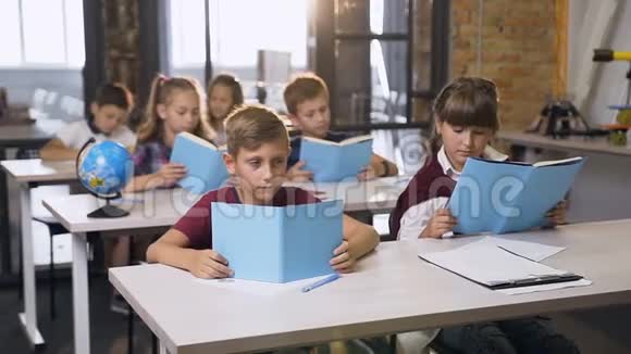 可爱的小男孩和小女孩坐在书桌前互相看着对方微笑着看着课上的书视频的预览图