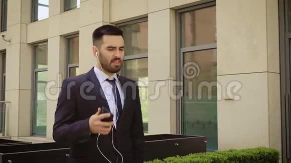 年轻的商人带着太阳镜在户外听智能手机上的音乐跳舞他走在办公室附近视频的预览图