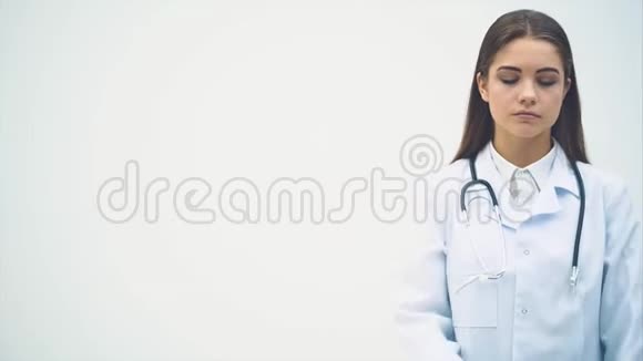 年轻的女医生出现在白色的背景下看着镜头微笑着摆姿势双手合十视频的预览图