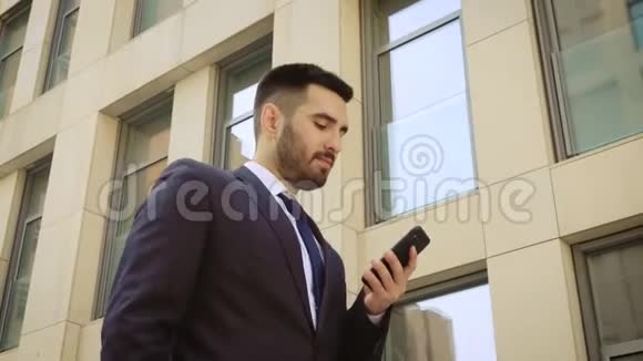 在现代人的背景下一位穿着智能手机的微笑商人在散步时近距离观看视频的预览图