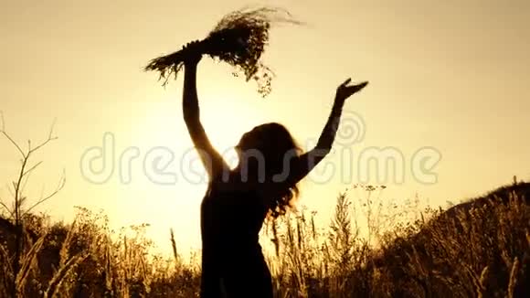 可爱的女孩挥舞着一束野花在夕阳下的夏日户外剪影快关门4K视频的预览图