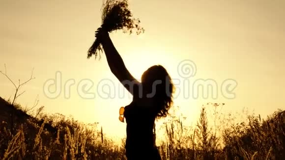 女孩在露天的夕阳下捧着一束野花嗅着它举起它剪影快关门4K视频的预览图