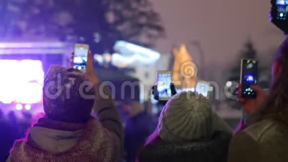圣诞音乐会上的人群在舞台附近举起双手录制视频并在智能手机相机上拍照青年视频的预览图