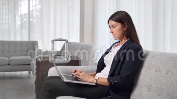忙碌的年轻女商人在出差期间用笔记本电脑坐在沙发上视频的预览图