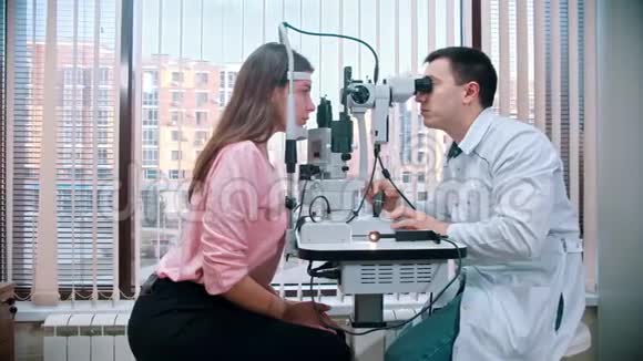 眼科治疗年轻漂亮的女人在宽敞的橱柜里用特殊的设备检查她的视力视频的预览图