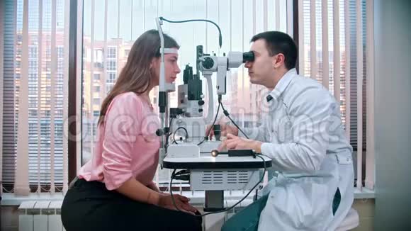 眼科治疗年轻漂亮的女人在宽敞的橱柜里用特殊的设备检查她的视力视频的预览图
