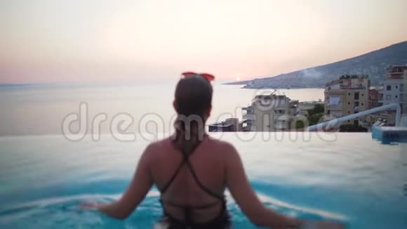 女人在游泳池水疗享受日落在海上豪华度假旅行在希腊欧洲穿比基尼的女孩视频的预览图
