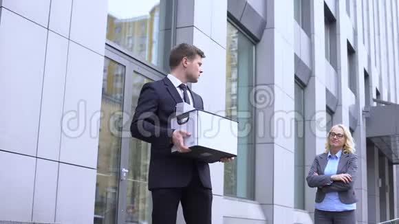 可悲的男经理带着装盒看着幸灾乐祸的女老板公司解雇视频的预览图