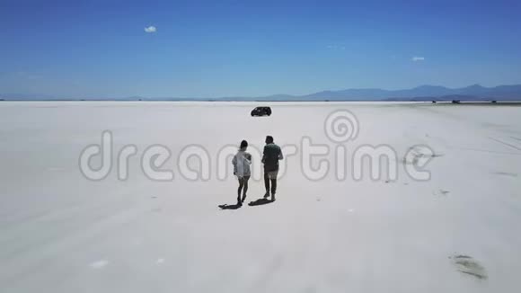 无人机跟着男人和女人牵着手在大气的盐漠湖景观中间朝汽车跑去视频的预览图