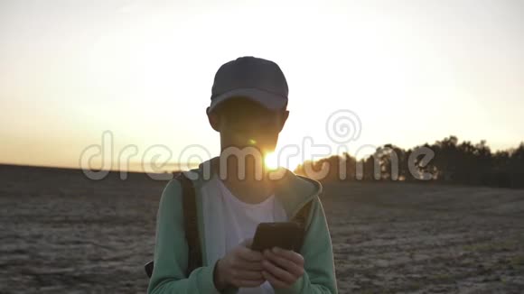 一个背着背包的有趣男孩的肖像日落时在户外使用电话旅行概念视频的预览图