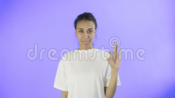 可爱的非裔美国女孩在工作室的紫罗兰背景上用两个拇指和微笑表现得很好视频的预览图