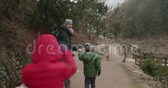 穿着红色夹克衫的小女孩蹦蹦跳跳地在森林小径上追赶一个女人和一个小男孩视频的预览图