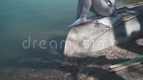 春天的一天一个年轻的女人坐在湖边的一艘旧船上在大自然中放松摄像机从下往上视频的预览图