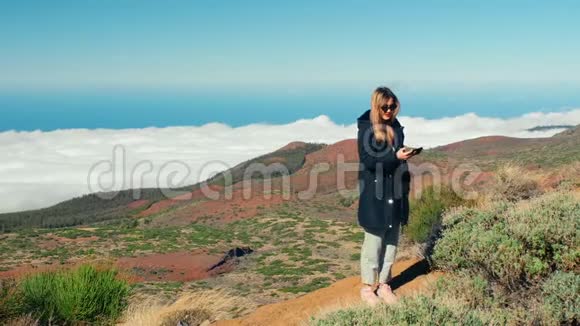 迷人的金发女人用智能手机自拍有云海和森林的美丽景观视频的预览图