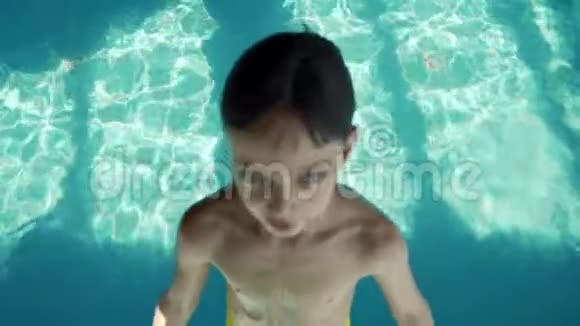 九岁的男孩掉进游泳池里带着蓝色的水溅向不同的方向飞行慢动作视频的预览图