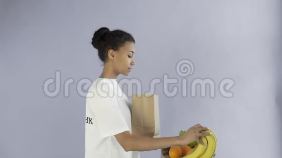 快乐的女人用灰色背景的有机健康蔬菜和水果装入纸袋视频的预览图
