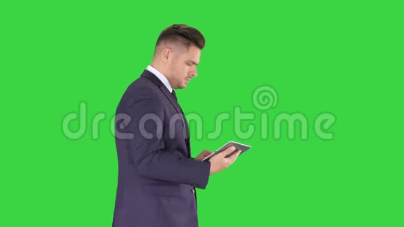 优雅的年轻商人使用他的电脑平板电脑而走在绿色屏幕Chroma键视频的预览图