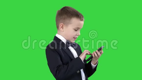 年轻男孩穿着优雅的西装在绿色屏幕上玩手机Chroma键视频的预览图